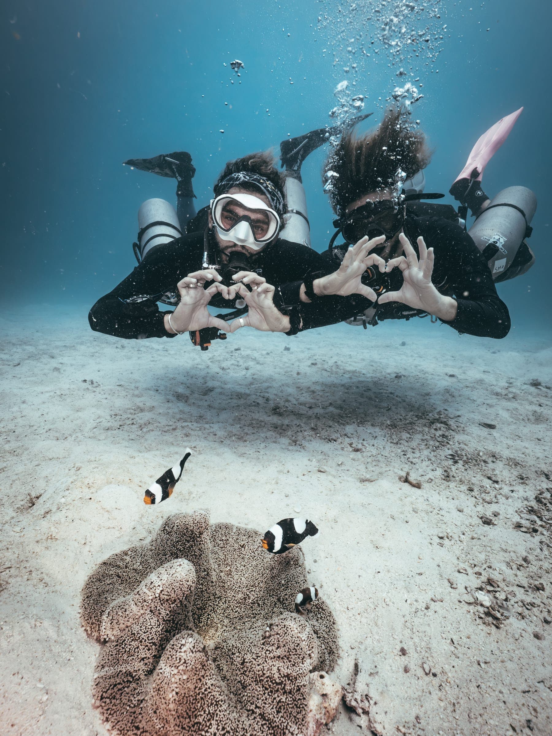 Onyx Divers instructors making a heart sign underwater with clownfish